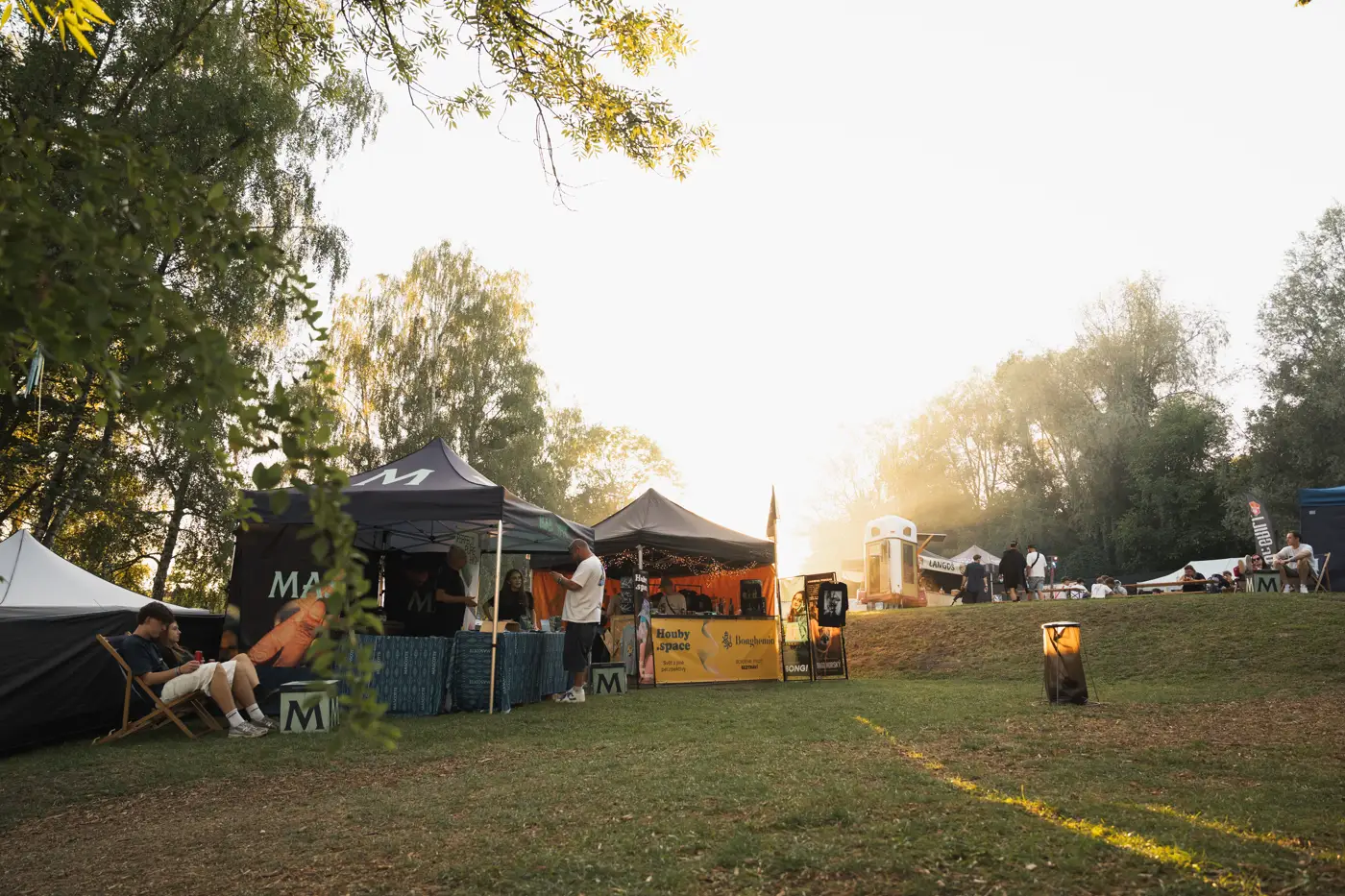 Festival TLAK 2026 — Areál festivalu se stánky při západu slunce